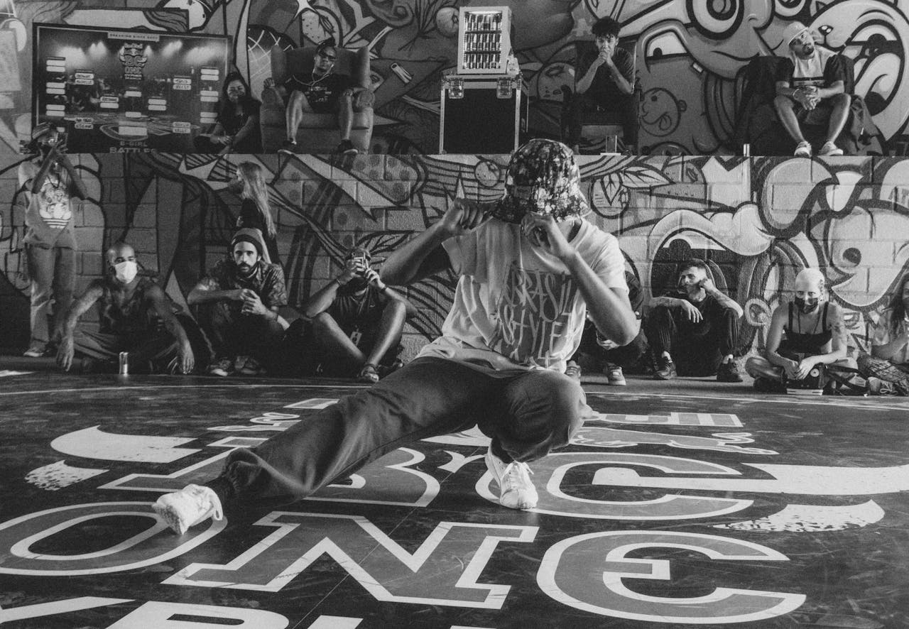 home-hero A breakdancer performs energetically in front of a graffiti wall, surrounded by an audience.