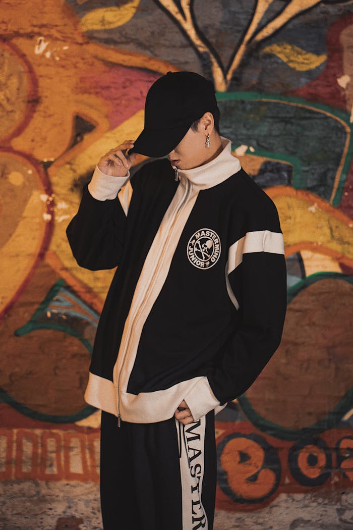 Stylish adult posing with hat and streetwear against vibrant graffiti backdrop.